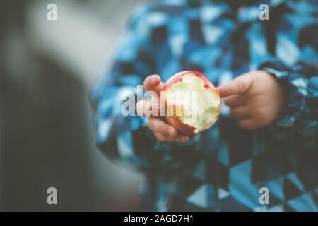 Nahaufnahme der Hand eines Kindes, das einen halb gefressenen roten Apfel hält Mit einem verschwommenen Hintergrund Stockfoto