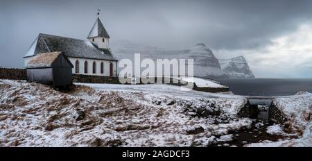 Weiße Kirche in verschneiten Vidareidi Dorf mit Bordoy und Kunoy Inseln im Hintergrund, Färöer Inseln Stockfoto