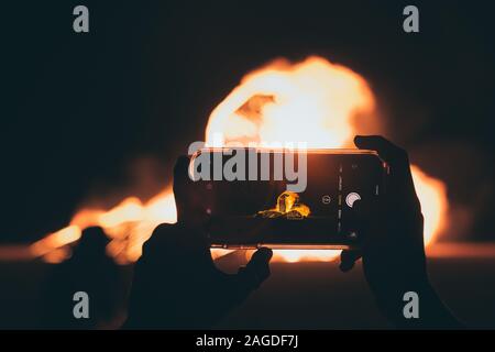Person, die mit einem Smartphone ein Bild vom Lagerfeuer gemacht hat Nachts Stockfoto