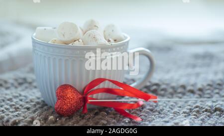 Rotes Herz auf einem Stick Neben große Tasse mit warmen Kaffee oder Tee. Morgen am Valentinstag. Angenehme Überraschung für Urlaub. Schale auf gestrickt Grau na Stockfoto