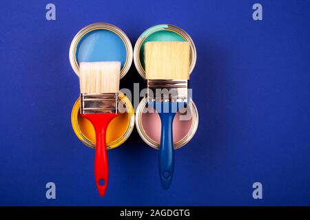 Vier offene Farbdosen mit Bürsten auf blauem Hintergrund. Gelb, Blau, Pink, Türkis Farben. Ansicht von oben. Stockfoto