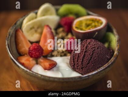 Köstliche Schüssel mit Joghurt, Eis, Nüssen und frischem Obst auf einer Holzoberfläche Stockfoto