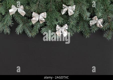 Weihnachten Grenze mit Tannenzweigen und Silber Bogen auf einem schwarzen Hintergrund. Frohes neues Jahr. Platz für Text. Winter Konzept. Grußkarte. Stockfoto