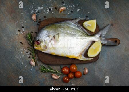 Frische butterfische Fisch mit Kräuter Gewürze Rosmarin Tomaten und Zitronen auf Holz Schneidebrett und schwarze Platte Hintergrund/Raw schwarz butterfische Fisch Stockfoto