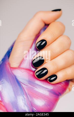 Hände mit schwarzen Maniküre holding Schleim in Blau und Rosa leuchtende Farben Stockfoto