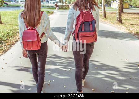 Zwei Mädchen im Teenageralter in der Stadt auf Herbst Tag im Sommer zu Fuß, halten Sie Hände, Blick von der Rückseite, legere Kleidung, Jeans und einen Pullover, zu Fuß nach Schule und Hochschule Stockfoto