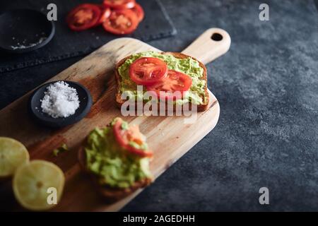 High-Angle Schuss von zwei Toast mit Avocado und Tomaten Mit Salz und Zitrone auf einem Schneidebrett Stockfoto