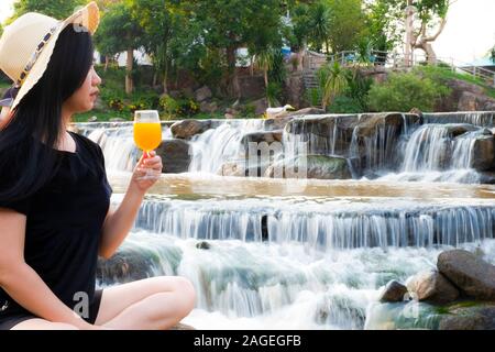 Portrait Frauen Hand halten frisch gepressten Orangensaft in Glas mit entgratet Wasserfall Hintergrund Stockfoto