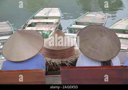 Menschen in konischen Hüten witting in der Nähe der Boote im See in Ninh Binh, Vietnam Stockfoto