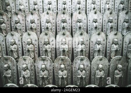 Reihe von buddhistischen Jizo-Statuen in einem Tempel in Japan Mit Hieroglyphen auf ihnen Stockfoto
