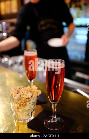 Kir Royale Cocktail Aperitif, serviert auf einem Bartresen mit Popcorn und ein Barkeeper im Hintergrund. Paris. Frankreich Stockfoto