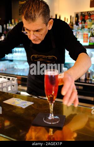 Kir Royale Cocktail Aperitif, serviert auf einem Bartresen mit Popcorn und ein Barkeeper im Hintergrund. Paris. Frankreich Stockfoto