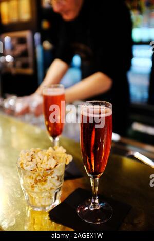 Kir Royale Cocktail Aperitif, serviert auf einem Bartresen mit Popcorn und ein Barkeeper im Hintergrund. Paris. Frankreich Stockfoto