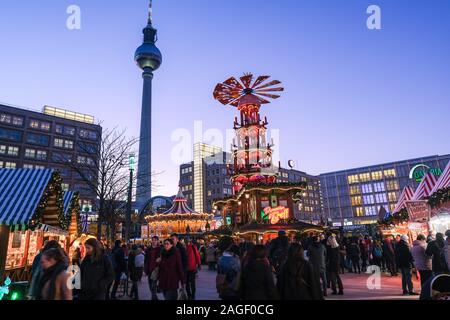 18 Dezember 2019, Berlin: Der Weihnachtsmarkt am Alexanderplatz mit einer großen Pyramide in den Abend in der blauen Stunde. Im Hintergrund das alexanderhaus (L-R), der Fernsehturm, das Berolinahaus und das Kaufhaus Galeria Kaufhof. Foto: Jens Kalaene/dpa-Zentralbild/ZB Stockfoto