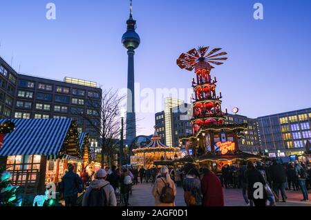 18 Dezember 2019, Berlin: Der Weihnachtsmarkt am Alexanderplatz mit einer großen Pyramide in den Abend in der blauen Stunde. Im Hintergrund das alexanderhaus (L-R), der Fernsehturm, das Berolinahaus und das Kaufhaus Galeria Kaufhof. Foto: Jens Kalaene/dpa-Zentralbild/ZB Stockfoto