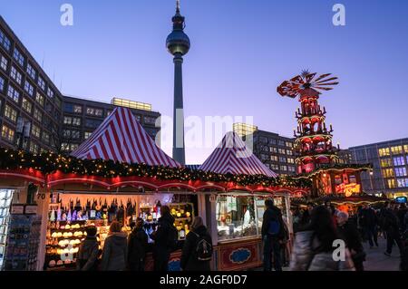 18 Dezember 2019, Berlin: Der Weihnachtsmarkt am Alexanderplatz mit einer großen Pyramide in den Abend in der blauen Stunde. Im Hintergrund das alexanderhaus (L-R), der Fernsehturm, das Berolinahaus und das Kaufhaus Galeria Kaufhof. Foto: Jens Kalaene/dpa-Zentralbild/ZB Stockfoto