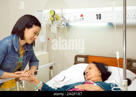 Südostasiatische Enkelin Besuch ihrer kranken Großmutter in der Klinik. Halten sich an den Händen. Stockfoto