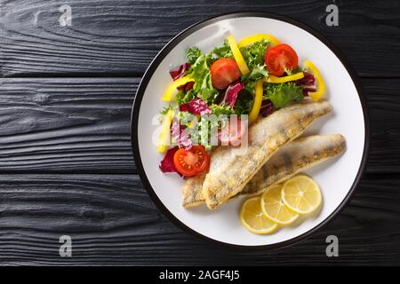 Süßwasser Fisch Filet vom Zander gebraten mit frischem Gemüse und Zitrone close-up in einem Teller auf dem Tisch. Horizontal oben Ansicht von oben Stockfoto