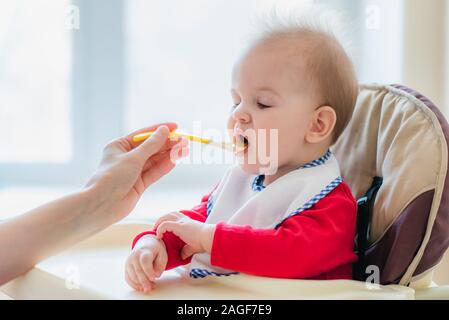 Kleines Kind sitzt auf einem Stuhl und essen mit Löffel Stockfoto