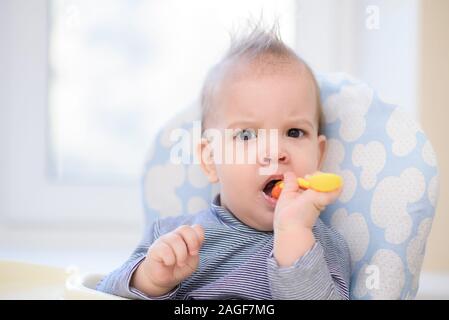 Kleines Kind sitzt auf einem Stuhl und essen mit Löffel Stockfoto