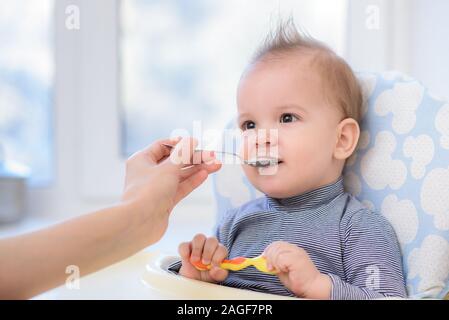 Kleines Kind sitzt auf einem Stuhl und essen mit Löffel Stockfoto