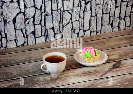 Nachtisch, eine Tasse schwarzen Kaffee und eine Platte mit einem Korb von Kuchen mit Protein Creme in Form von Rosen sind auf einen hölzernen Tisch gegen eine Mauer aus Stein. Clos Stockfoto