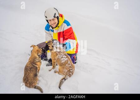 Junge männliche Snowboarder spielt mit Welpen bei einem Skigebiet im Winter Stockfoto