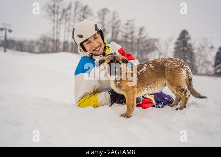 Junge männliche Snowboarder spielt mit Welpen bei einem Skigebiet im Winter Stockfoto