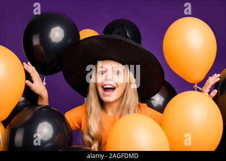 Foto von verrückte kleine Hexe Lady halloween party versteckt zwischen vielen Luftballons angeregten Abend orange T-Shirt wizard Hut isoliert lila Farbe Stockfoto