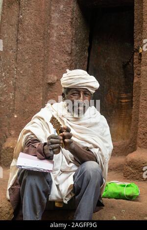 Äthiopien, Amhara-region, Lalibela, Arbatu Chirkos Ensessa, Biblia, lächelnd Priester in Neteld Schal gehüllt saßen draußen Kirche Tür Stockfoto