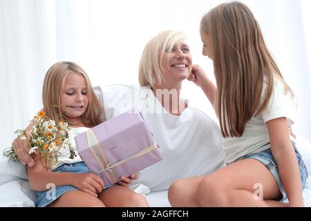 Glückliche Mutter mit Blumen und Geschenke sitzt mit ihren Töchtern auf dem Bett. Stockfoto