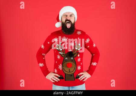 Frohe Weihnachten. bereit für Xmas Party. Frohes neues Jahr. winking Hipster lustig gestrickte Pullover. warme Kleidung in der kalten Winter. Saison Stimmung. bärtiger Mann Weihnachtsmütze Rot hinterlegt Stockfoto