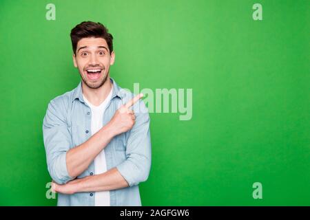 Foto fröhliche, positive Braunhaarige süß Mann zeigte auf leeren Raum zum Ausdruck schockiert Emotionen aufgeregt ekstatisch über grüne lebendige Farben isoliert Stockfoto