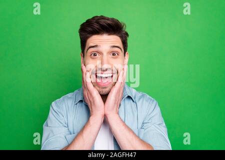 Nahaufnahme Foto von Super macho Kerl halten Arme auf Wangen auf unglaublich niedrigen Preisen tragen Casual denim Shirt über grüne Farbe isoliert Stockfoto