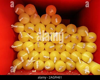 Gruppe von gelben Kerzen mit weißen Dochte in ein rotes Quadrat. Nahaufnahmen mit wenig Tageslicht. Stockfoto