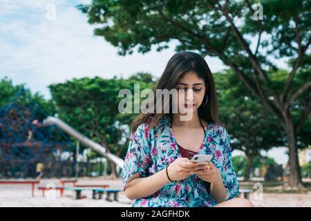 Ein langes Haar Asiatische indische weibliche Holding, und geben Sie auf dem Mobiltelefon mit Finger in outdoor Park Stockfoto