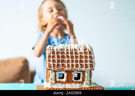 Süße kleine Junge isst Lebkuchenhaus und Spaß haben. Kid genießen Sie Weihnachtliche Traditionen. Kind brach ein Lebkuchenhaus. Backen und Kochen mit Kindern zu Weihnachten zu Hause. Weihnachten Konzept. Stockfoto