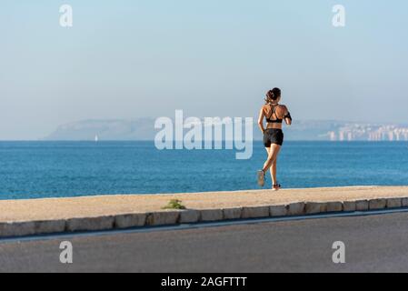 Frau Joggen am Strand mit einem Telefon, Alicante, Spanien. Stockfoto