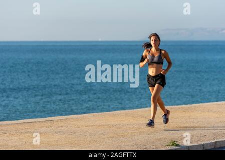 Frau Joggen am Strand mit einem Telefon, Alicante, Spanien. Stockfoto