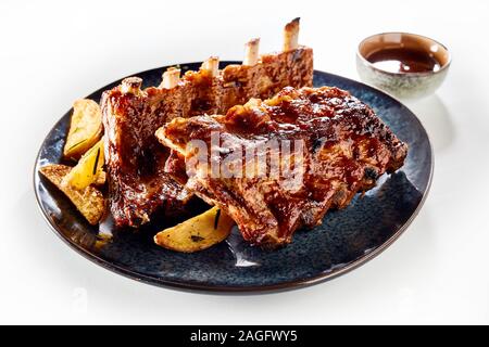 Zwei Racks von würzig mariniert gegrillte Rippchen mit bohnenkraut Rosmarin Potato Wedges auf schwarzem Teller über Weiß Stockfoto