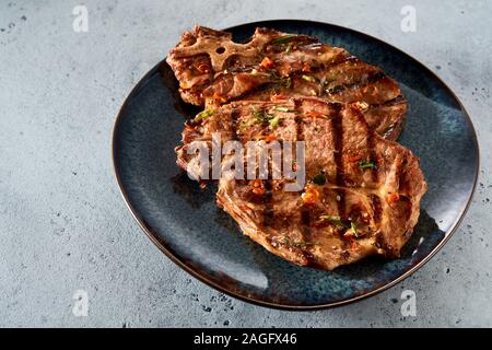 Zwei Schweinefleisch vom Grill, Steaks oder Knochen ribeye, mit Gewürzen und Chili Gewürz auf eine schwarze Platte auf einem grauen Hintergrund serviert. Stockfoto