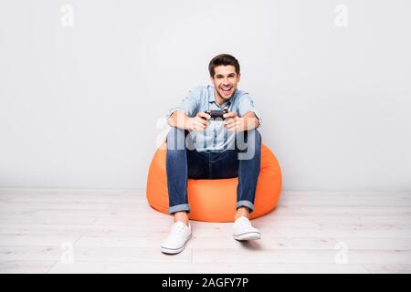 Volle Länge Körper Größe Foto von trendigen Mann zu spielen Videospiele tragen weiße Sneakers holding Joy Stick mit den Händen über die Farbe Grau isoliert süchtig Stockfoto