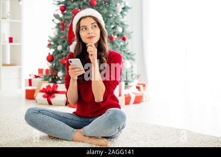 Foto Schöne charmante Süße hübsche süsse Frau mit roten Pullover Jeans Denim santa rote Kappe während Nachdenken über etwas mit Telefon in Stockfoto