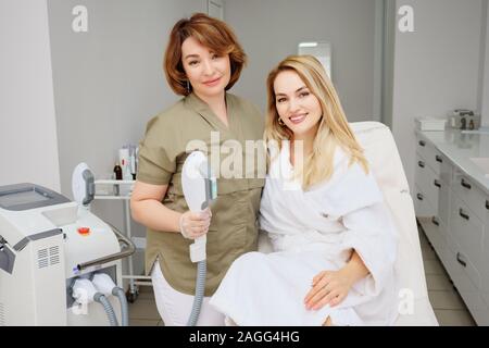 Beauty Klinik Mitarbeiter Moderne Lasertechnik für die Epilation in der Nähe von Client sitzen auf der Couch in der weißen Robe closeup Stockfoto
