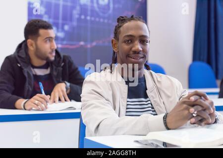 Lächelnd African American University männlicher Student in der Klasse sitzt an seinem Schreibtisch drehen lächeln in die Kamera. Stockfoto