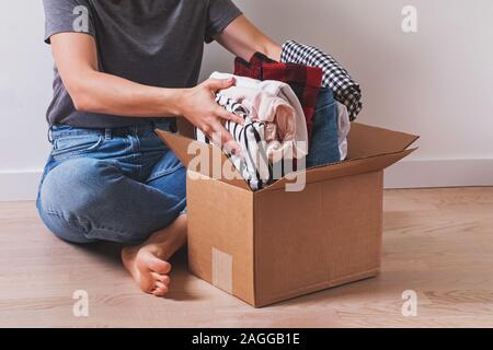 Nicht erkennbare Frau, Kleidung im Karton beim Sitzen auf dem Boden. Stockfoto