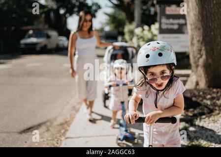 Mutter und Töchter spielen push Roller in der Nachbarschaft Stockfoto