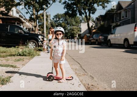 Kleinkind reiten auf Push Roller in Nachbarschaft, Familie im Hintergrund Stockfoto