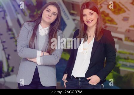 Zwei junge erfolgreiche Unternehmerinnen stehen in der Halle und auf der Suche nach der Kamera, zwei geschäftsfrauen posieren für werbliche Inhalte, während standin Stockfoto