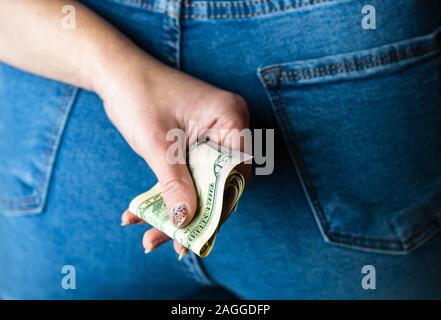 Frau Hand Geld nimmt, aus Jeans Gesäßtasche. Frau Geld versteckt hinter ihrem Rücken. Dollar Banknoten Nahaufnahme Stockfoto